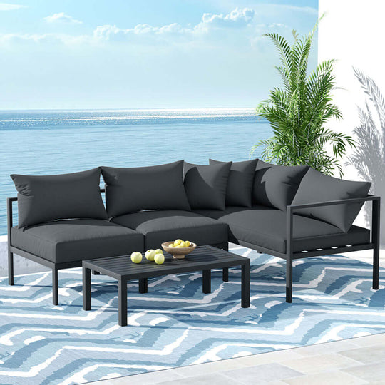 Gardeon 4-seater outdoor aluminium sofa set in charcoal with coffee table by the beach, offering affordable luxury for summer.