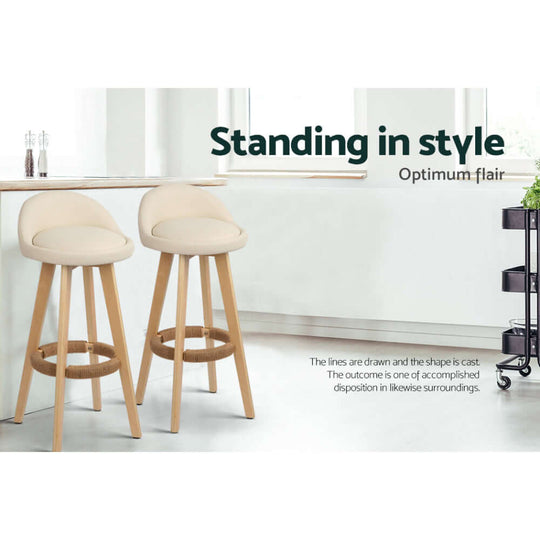 Stylish beige padded leather bar stools with wooden legs standing in a modern kitchen setting.