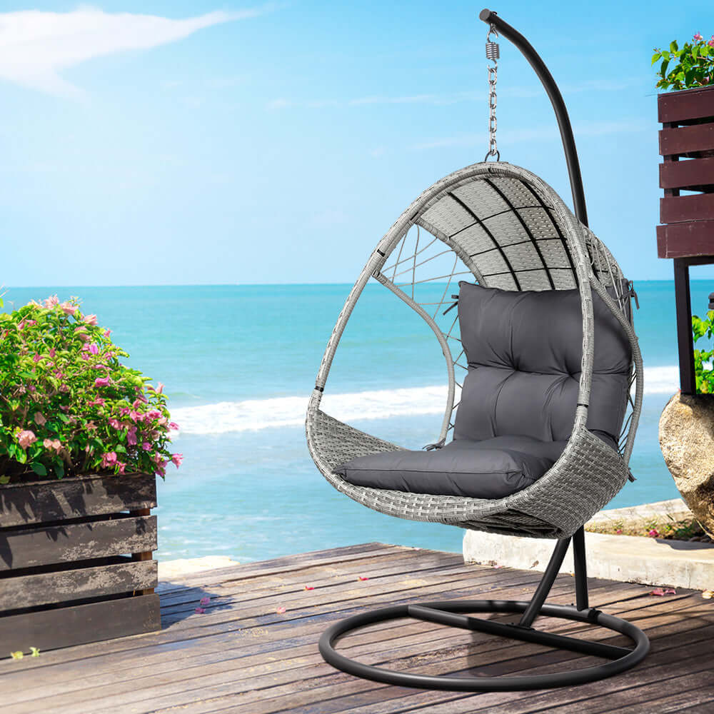 Gardeon affordable light grey egg swing chair on wooden patio by beach, featuring cozy cushions and sturdy stand.