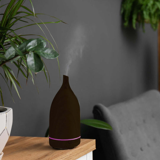 Milano Decor 100ml Ultrasonic Aroma Diffuser in dark wood with steam, set on a wooden table with plants in background.