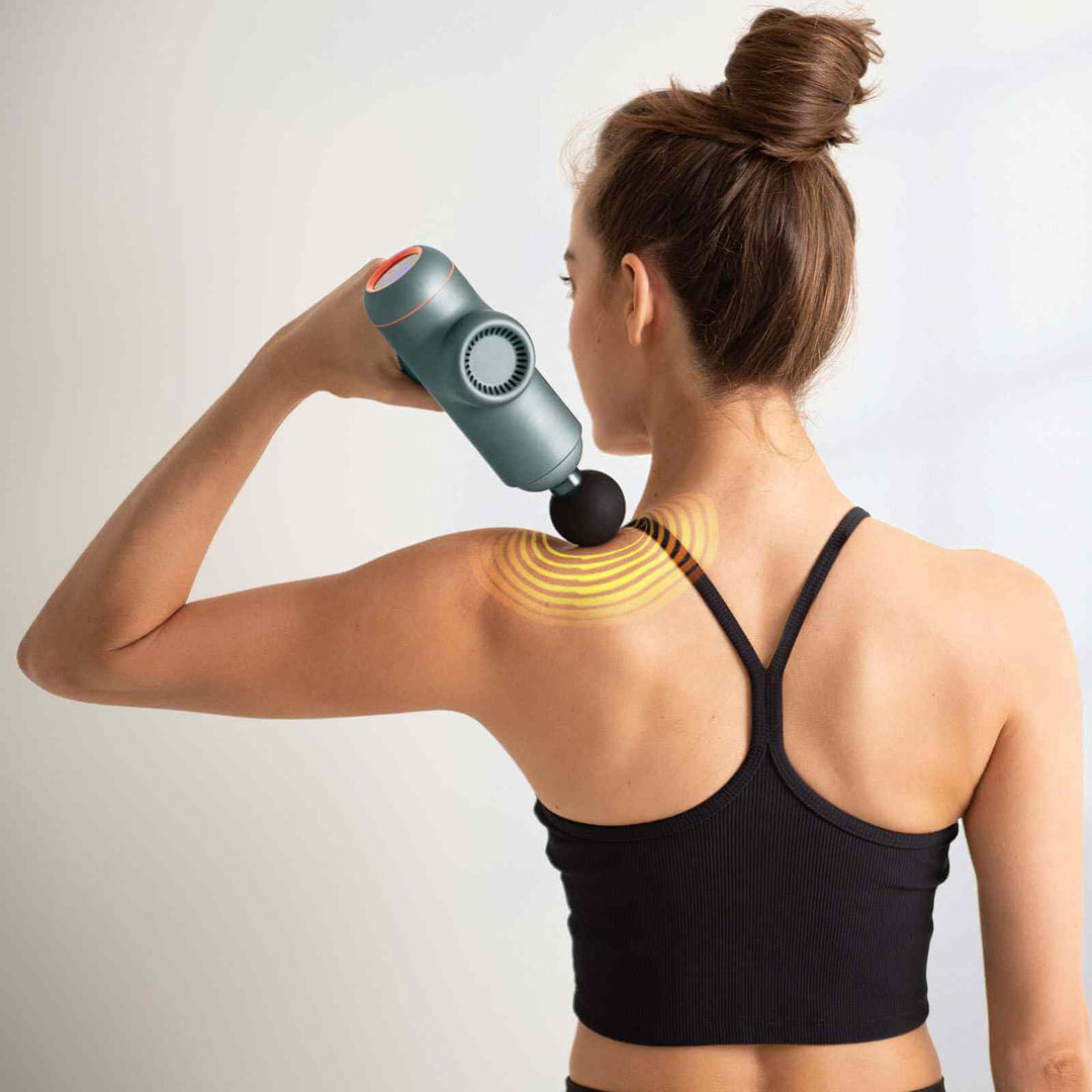 Woman using FitSmart LED Power-X Massage Gun on her shoulder for muscle relief and recovery in a stylish black tank top.