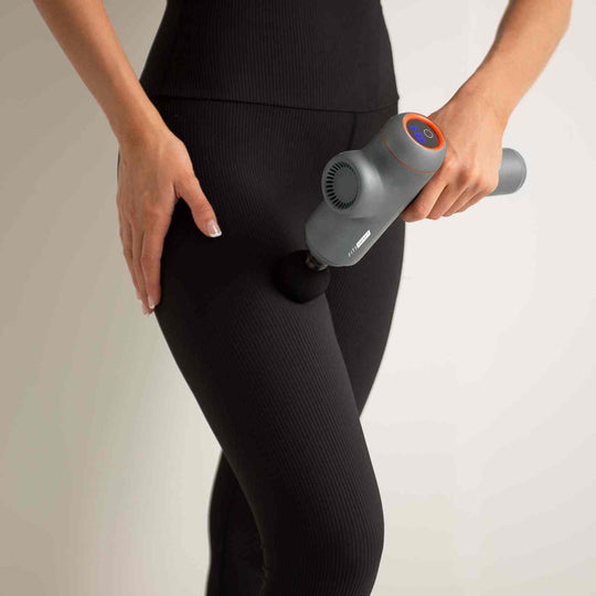 Woman using FitSmart Power-X Massage Gun on thigh, demonstrating effective muscle relief and vibration therapy in grey design.