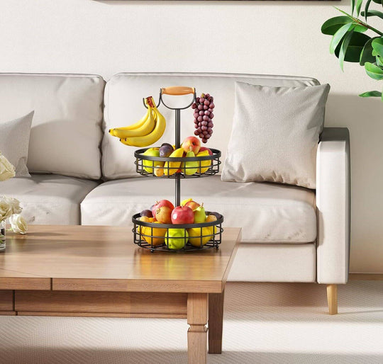 2-tier fruit basket with wood handle and banana hanger on a coffee table, showcasing colorful fruits in a stylish kitchen setting.