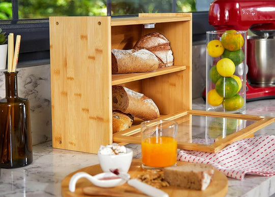 Double layer bamboo bread box on kitchen counter with rolls, muffins, and a transparent window, showcasing affordable quality.