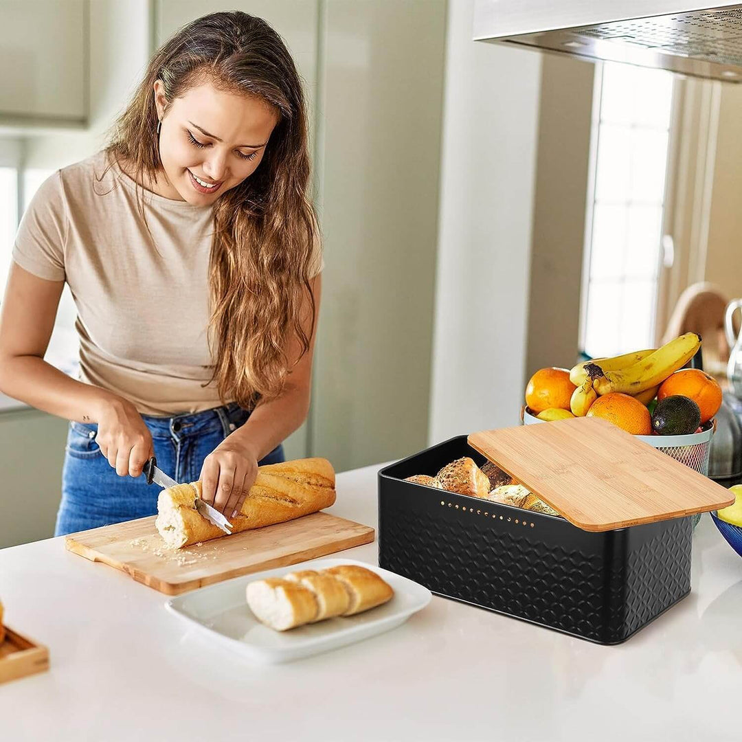 Woman using a stylish black bread bin with bamboo lid as a chopping board in a modern kitchen.