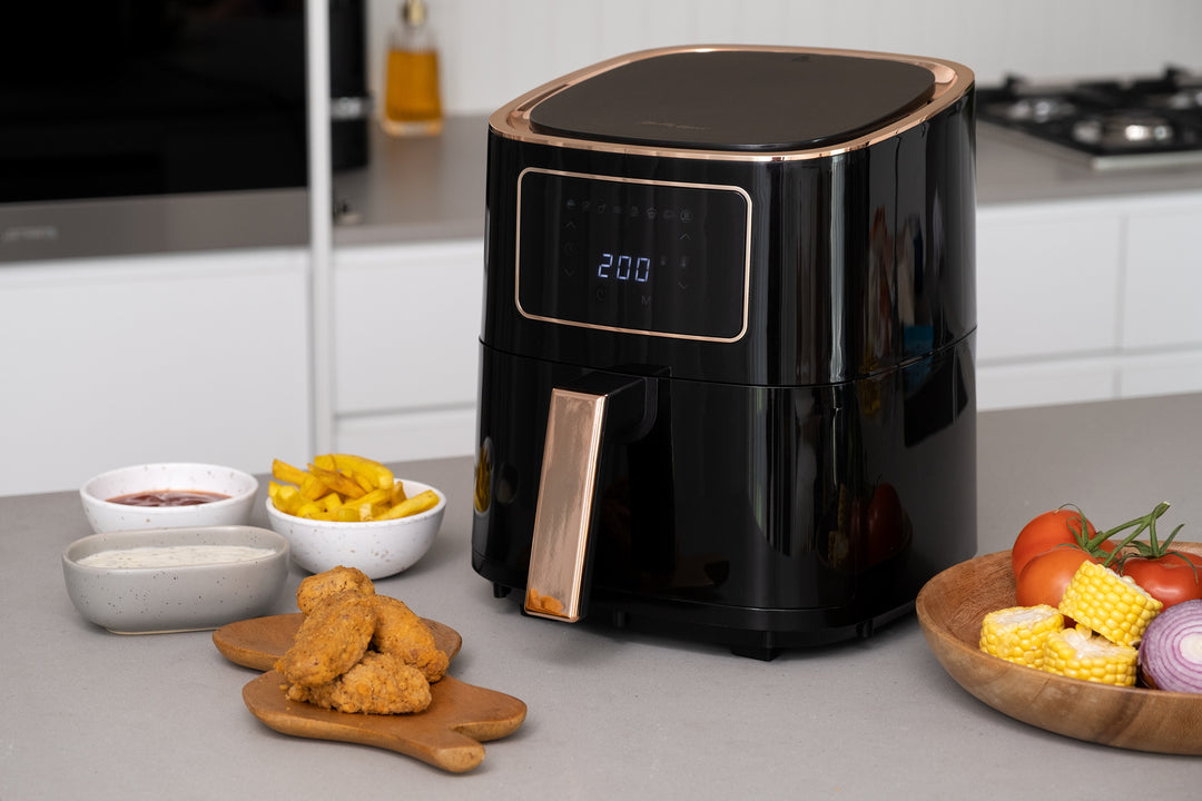 Modern black 7L digital air fryer with LED display, surrounded by cooked food, on a kitchen counter.