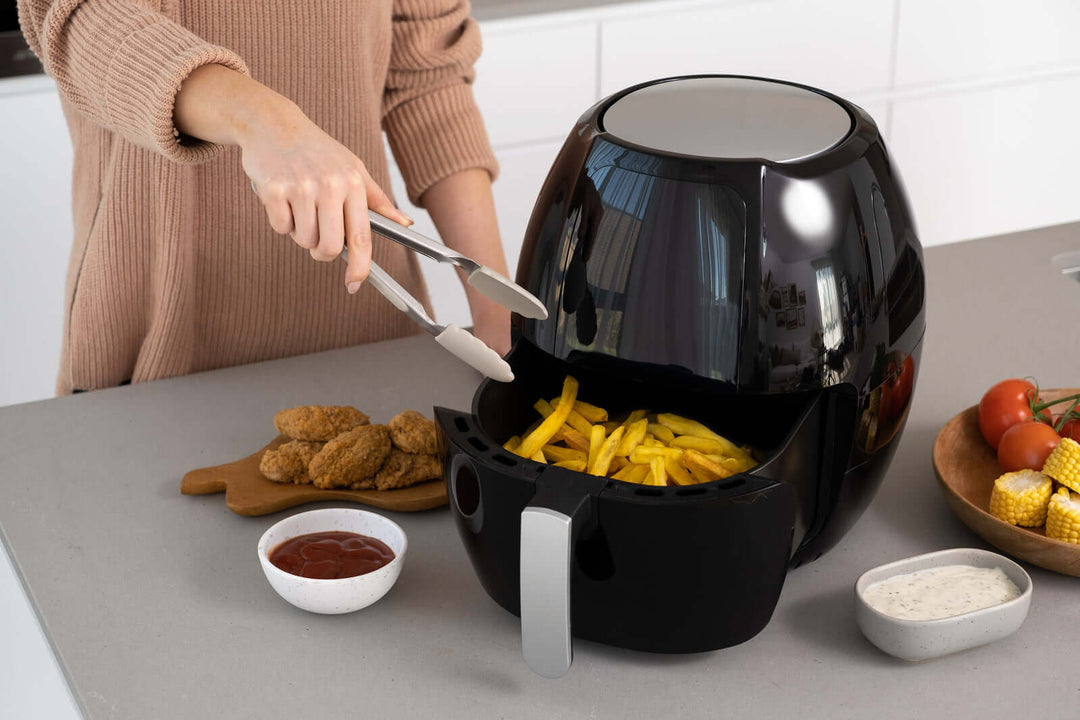 Cooking fries and chicken in 8L digital air fryer with tongs in modern kitchen for healthy, delicious meals.