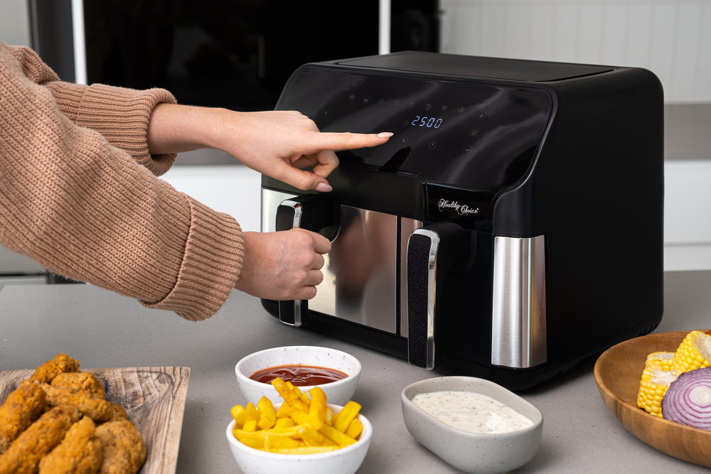 Person using the digital control panel on the 10L Digital Dual Zone Air Fryer to cook crispy fries and chicken wings in a modern kitchen