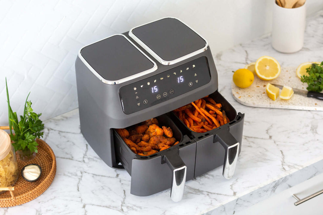 Dual Zone Digital Air Fryer with 2 non-stick cooking baskets on a marble countertop, displaying cooking programs, lemons, and herbs in the background