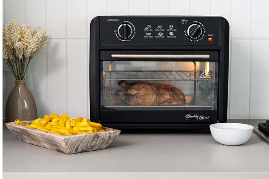 Black 23L air fryer oven cooking a roast chicken with a side of fries on the countertop