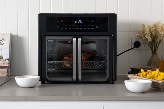 25L Air Fryer Convection Oven with 360 Cooking and French Doors on kitchen counter cooking a chicken, with surrounding bowls.