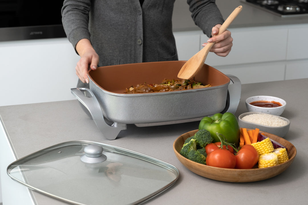 Person cooking in Copper Electric Fry Pan with vegetables, showcasing value furniture and affordable, quality kitchen appliances