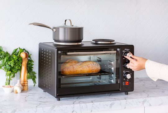 Person using portable oven with rotisserie cooking, baking bread. Affordable, quality value furniture appliance with 34L capacity.