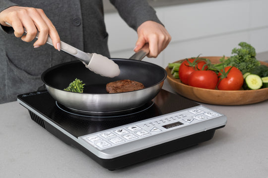 Cooking steak and vegetables on single electric induction cooker stove top.