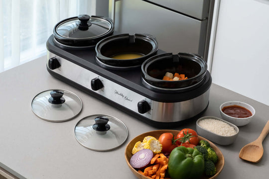 3-Pot Slow Cooker with three dishes, fresh vegetables, and sauces on a kitchen countertop for affordable and quality home cooking.