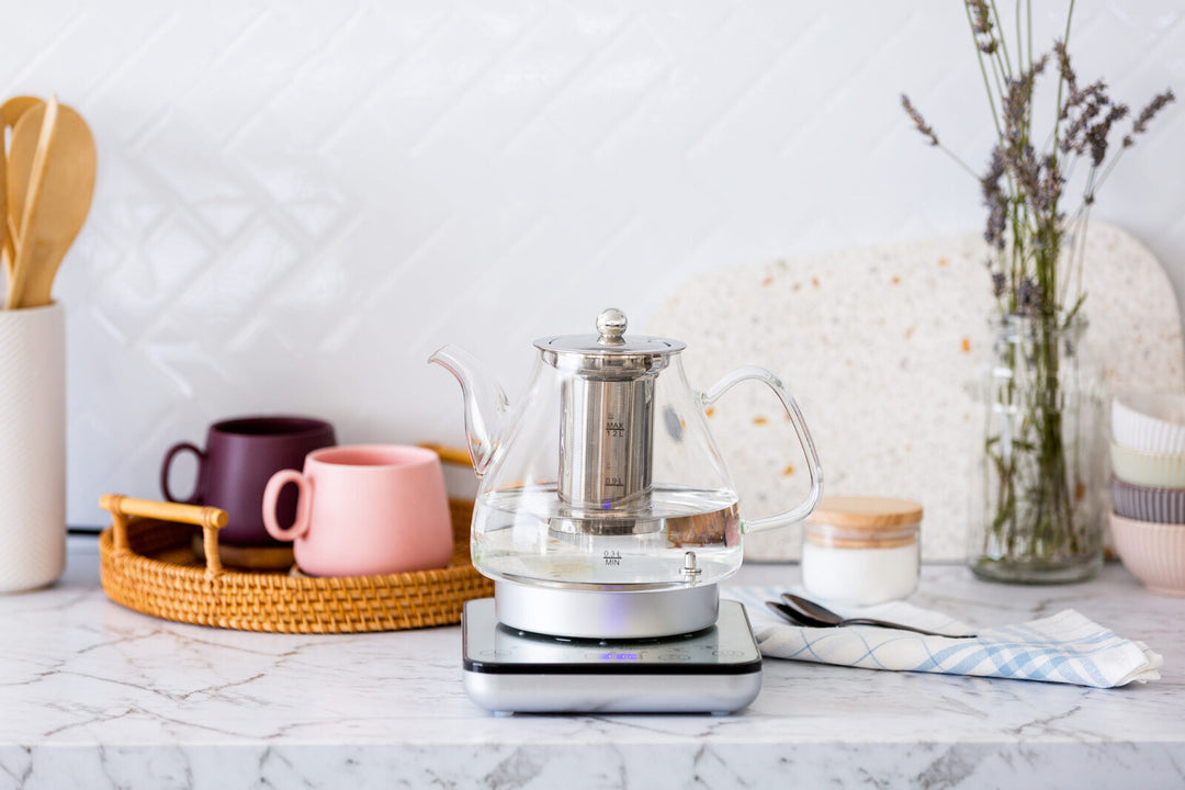 1.2L digital glass kettle with electric tea pot and infuser on a marble countertop, surrounded by mugs and kitchen decor.