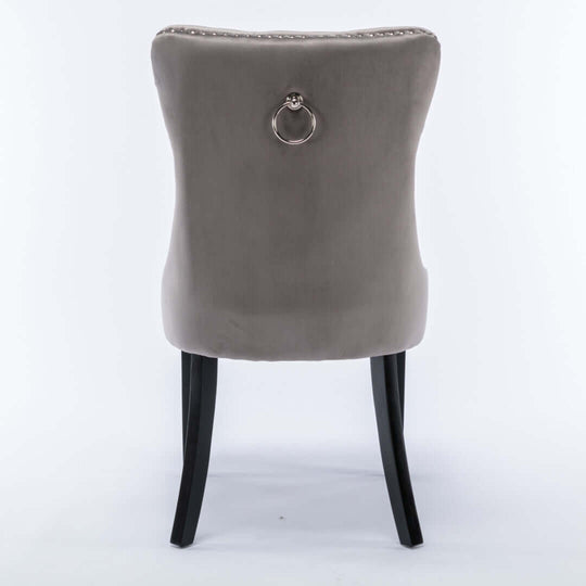 Back view of gray velvet dining chair with tufted upholstery, ring handle, solid wood legs, and stud trim detailing.