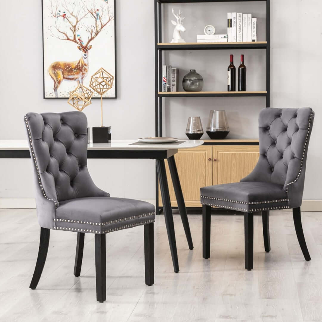 Gray velvet dining chairs with tufted backs, solid wood legs, and stud trim in a modern dining room setup.