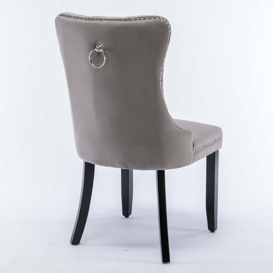 Gray velvet dining chair with solid wood legs, tufted back, stud trim, and ring accent, displaying a modern mid-century look.