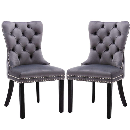 Two gray velvet upholstered dining chairs with tufted backs, solid wood legs, and stud trim detailing, perfect for a modern mid-century dining room.