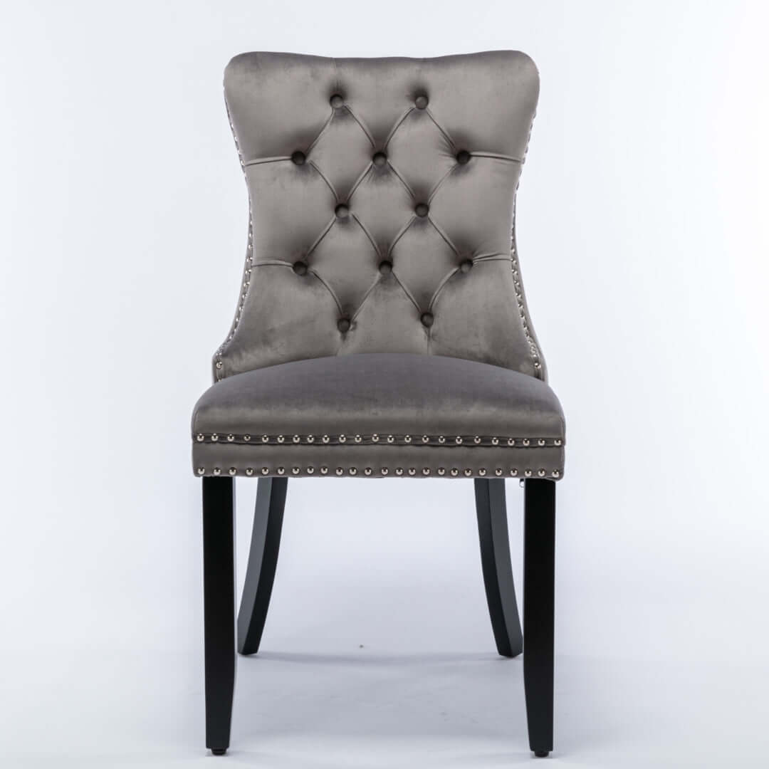 Gray velvet dining chair with tufted back, stud trim, and solid wood legs. Modern mid-century design with ergonomic high backrest.