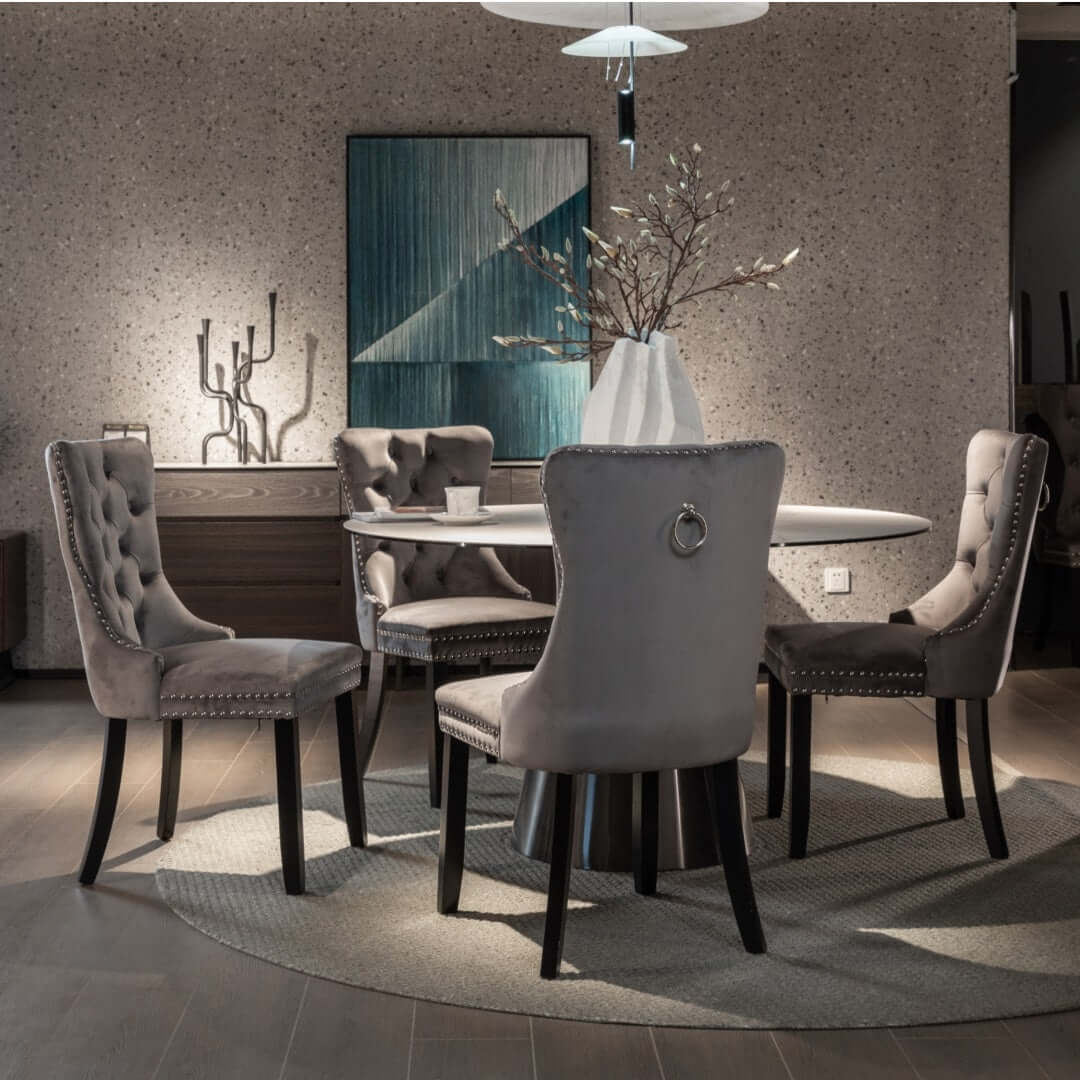 Gray velvet dining chairs with tufted backrests and stud trim around a modern dining table in contemporary dining room setup