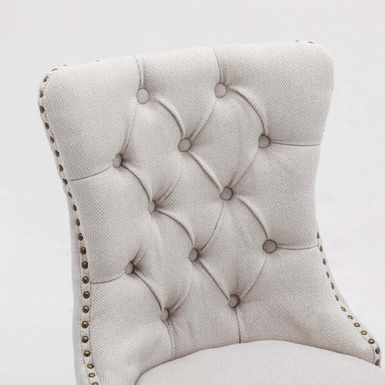 Close-up of beige button-tufted dining side chair with stud trim, showcasing elegant design and quality upholstery.