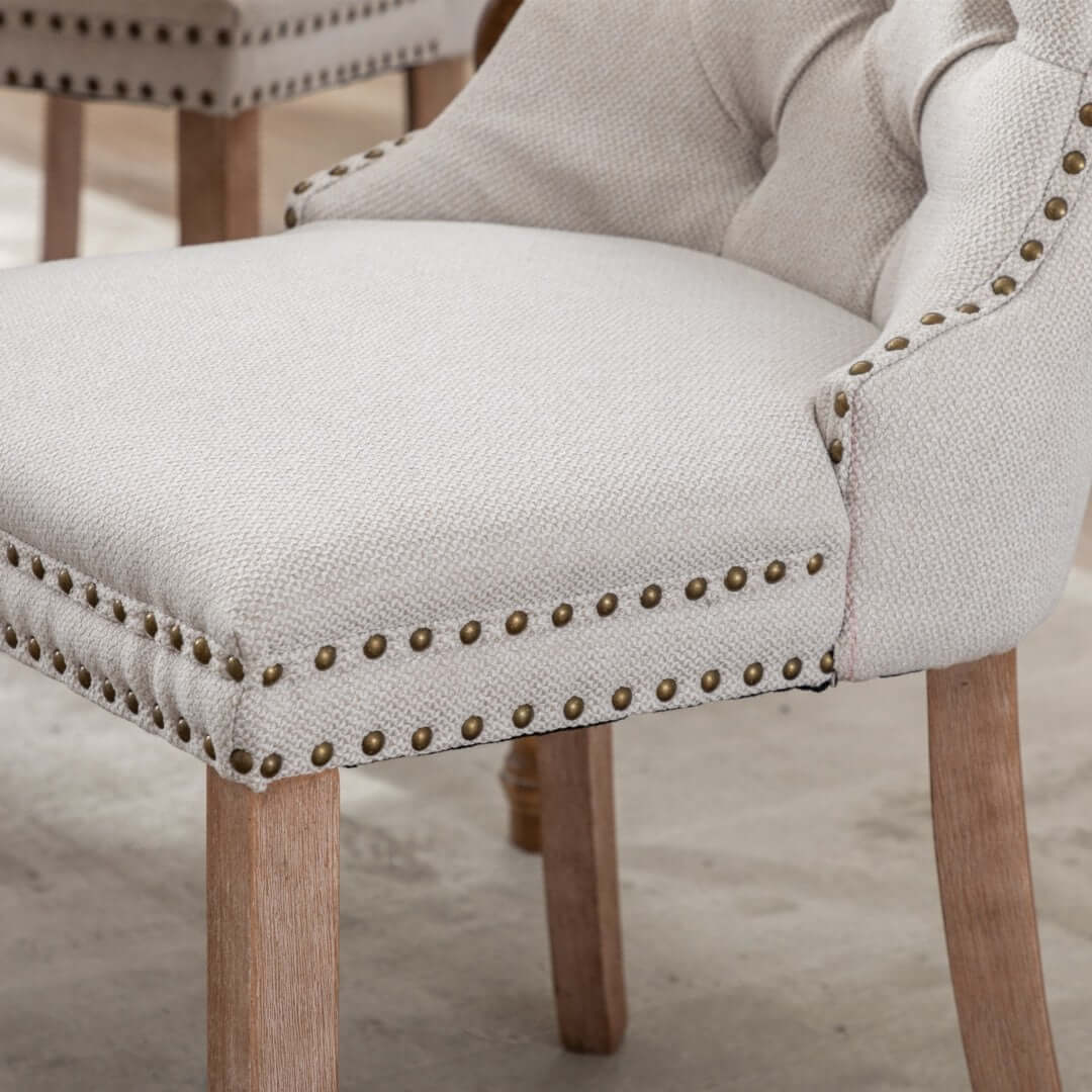 Beige button-tufted dining chair with stud trim, wooden legs, ideal for affordable luxury in dining or living spaces.