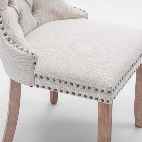 Close-up of elegant beige button-tufted upholstered dining chair with stud trim and wooden legs.