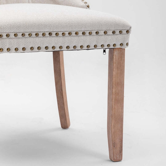 Close-up of a beige button-tufted dining chair with stud trim and wooden legs, showcasing elegant design and affordable quality.