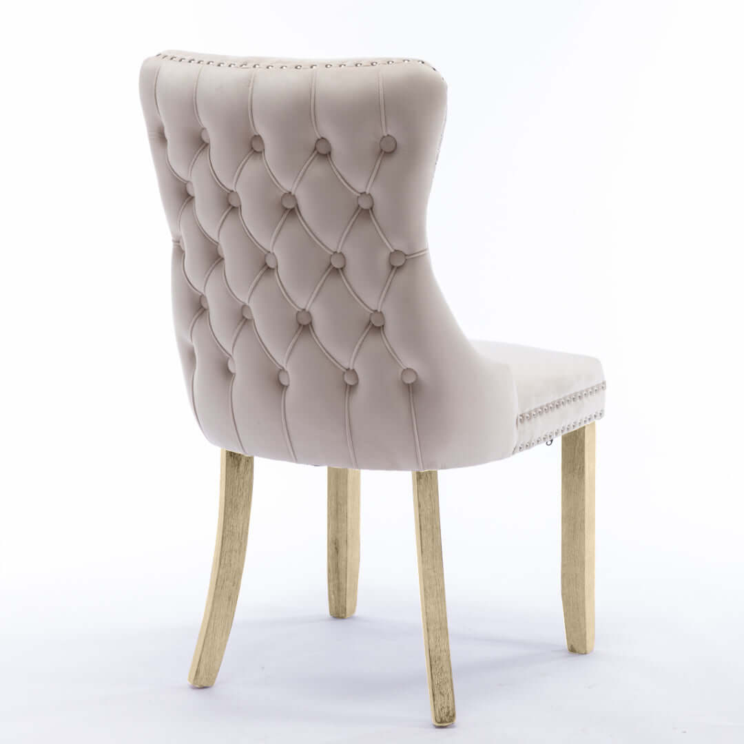 Velvet upholstered dining chair with tufted wingback, stud trim, and solid wood legs.