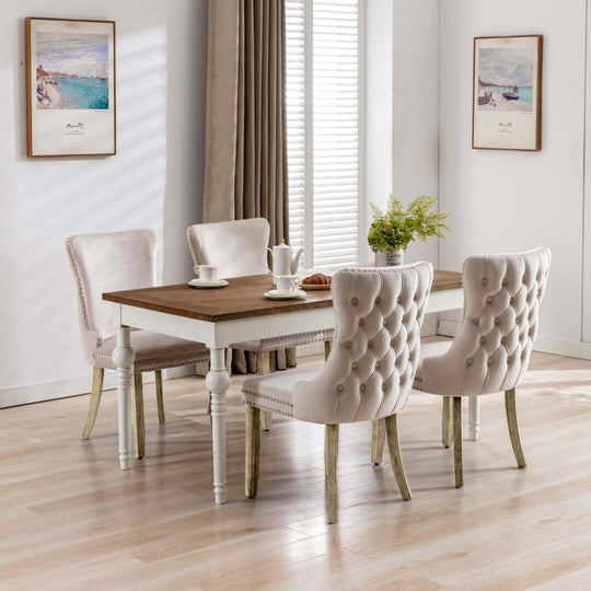 Velvet upholstered dining chairs with tufted wingback, stud trim, and solid wood legs in a modern kitchen setting with a wooden dining table.