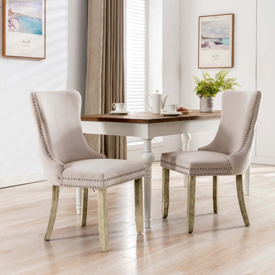 Velvet upholstered dining chairs with tufted wingback and solid wood legs around white kitchen table with sunlit window.