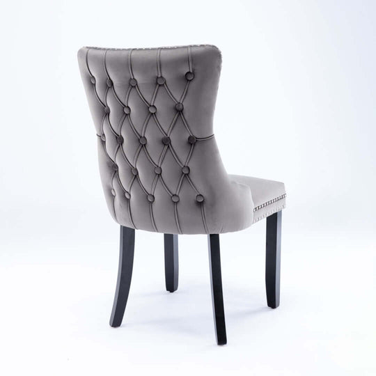 Velvet upholstered dining chair with tufted wingback design, solid wood legs, and stud trim from back view.