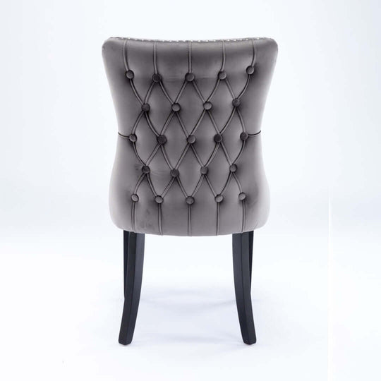 Back view of velvet upholstered dining chair with tufted wingback design, stud trim, and solid wood legs.