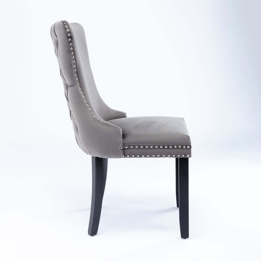 Side view of grey velvet upholstered dining chair with tufted wingback, stud trim, and solid wood legs. Ideal for modern kitchen decor.