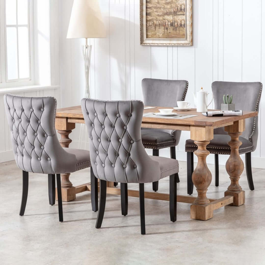 Velvet upholstered dining chairs with tufted wingback and studs trim around a wooden dining table in a modern kitchen setting