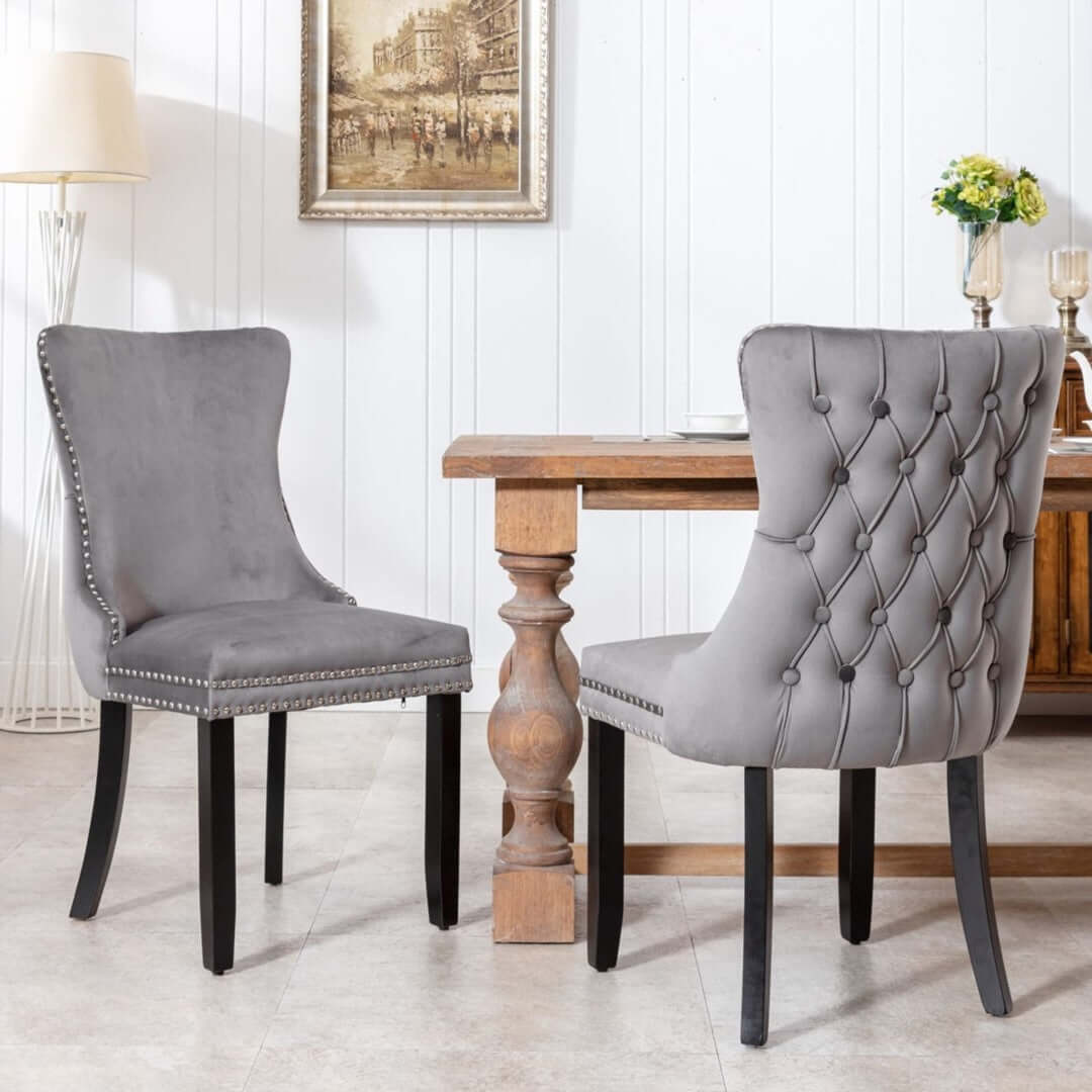 Velvet upholstered dining chairs with tufted wingback, studs trim, and solid wood legs in a kitchen setting.