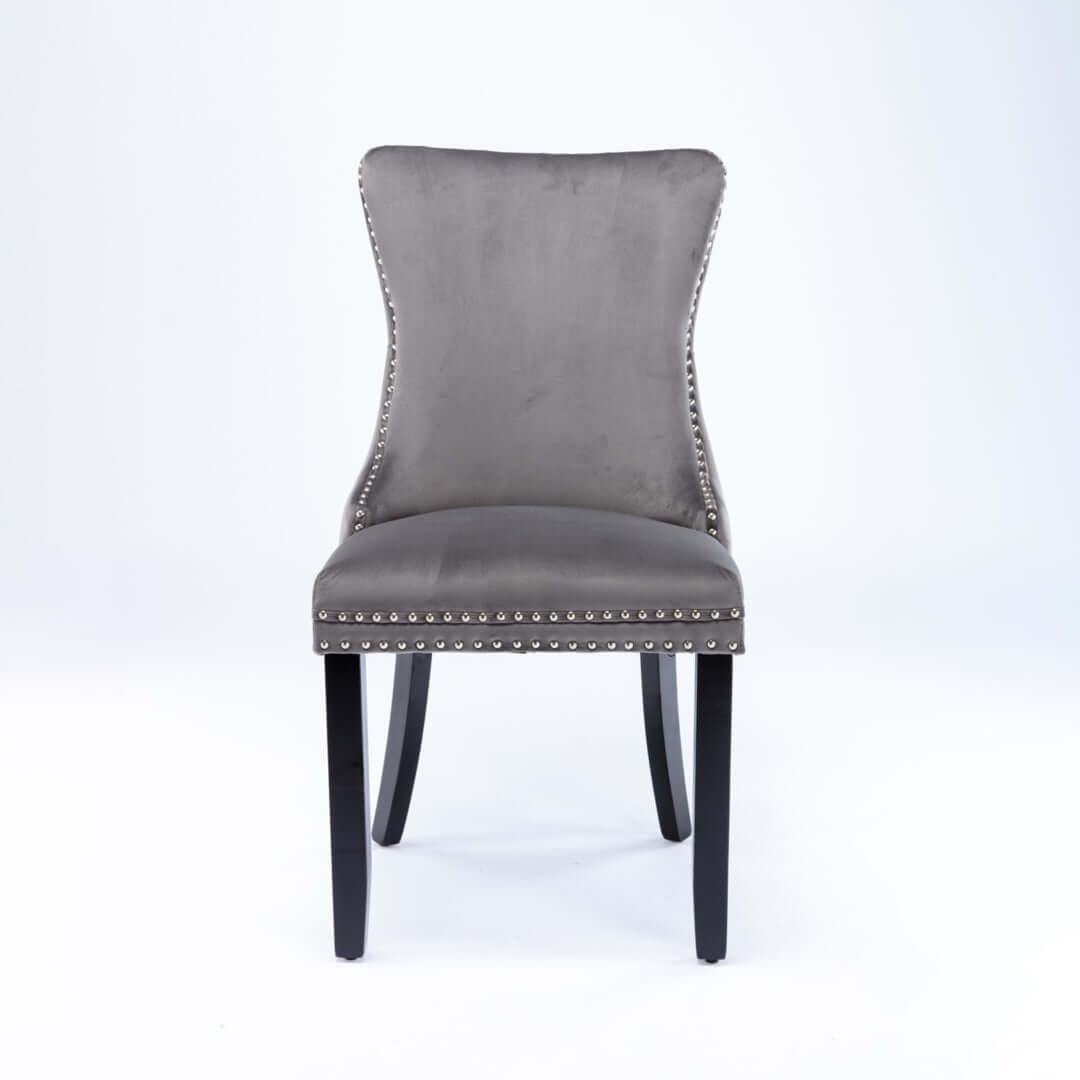 Velvet upholstered dining chair with tufted wingback design, stud trim, and solid wood legs suitable for kitchen or dining room decor.