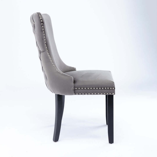 Velvet upholstered tufted wingback dining chair with studs trim and solid wood legs, side view.