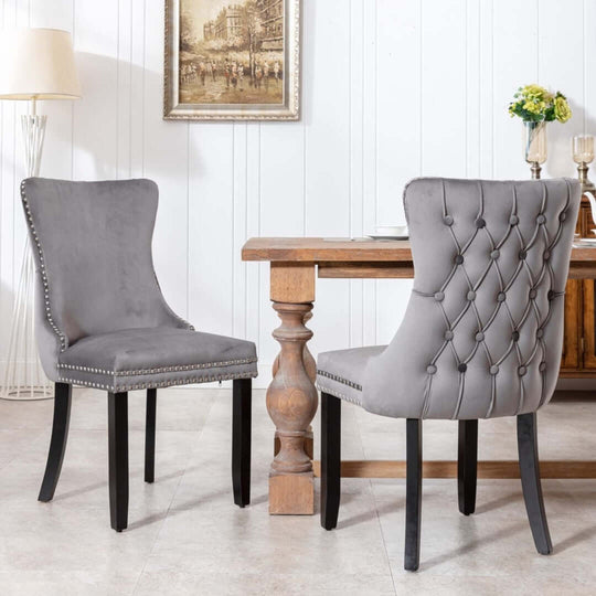 Elegant velvet upholstered dining chairs with tufted wingback design, studs trim, and solid wood legs in kitchen setting.