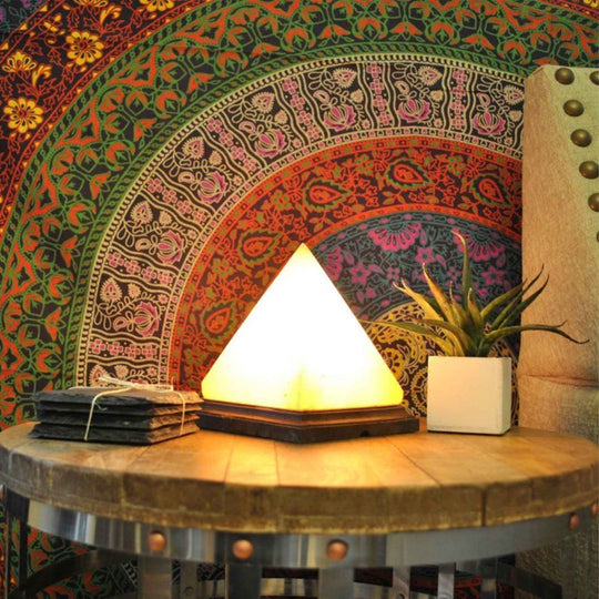 Pyramid Himalayan pink salt lamp on a wooden table, enhancing a colorful bohemian decor background. Affordable luxury for any space.