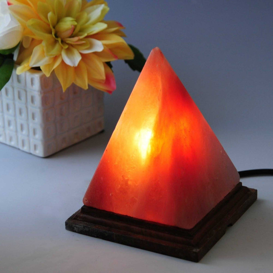 Handcrafted pyramid Himalayan pink salt lamp with warm glow on wooden base, perfect for affordable DIY home decor.