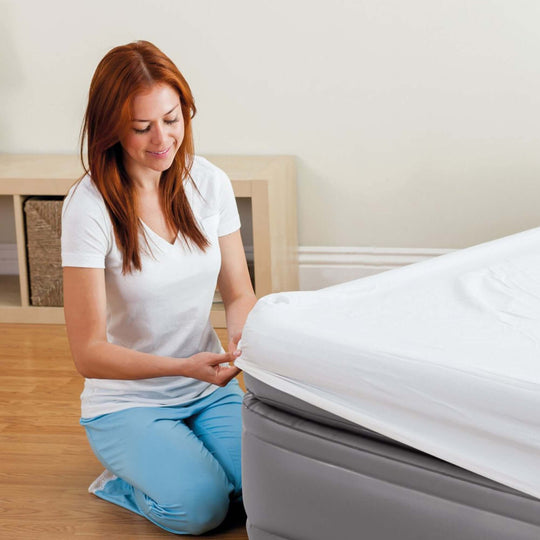 Woman adjusting fitted sheet on Intex Dura-Beam elevated air mattress for a quality sleep experience.