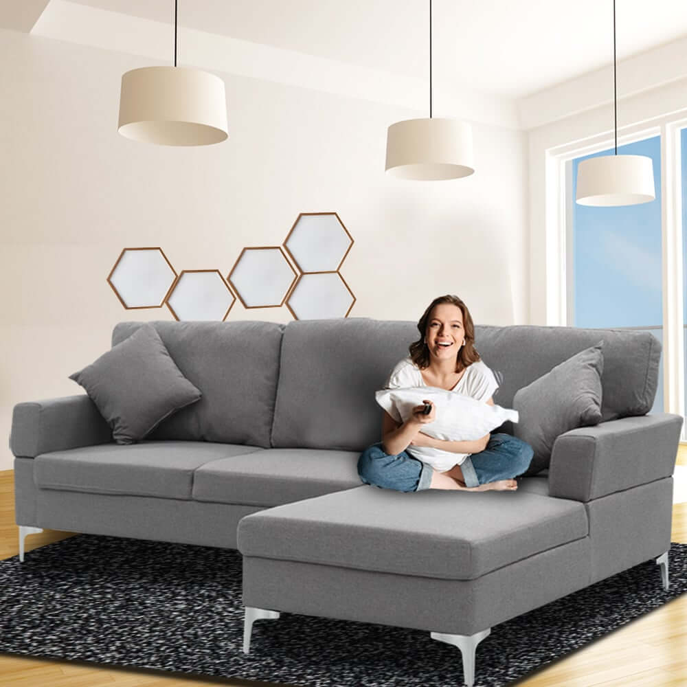 Woman relaxing on Sarantino dark grey 3 seater linen sofa with left chaise, showcasing affordable luxury in a modern living room.