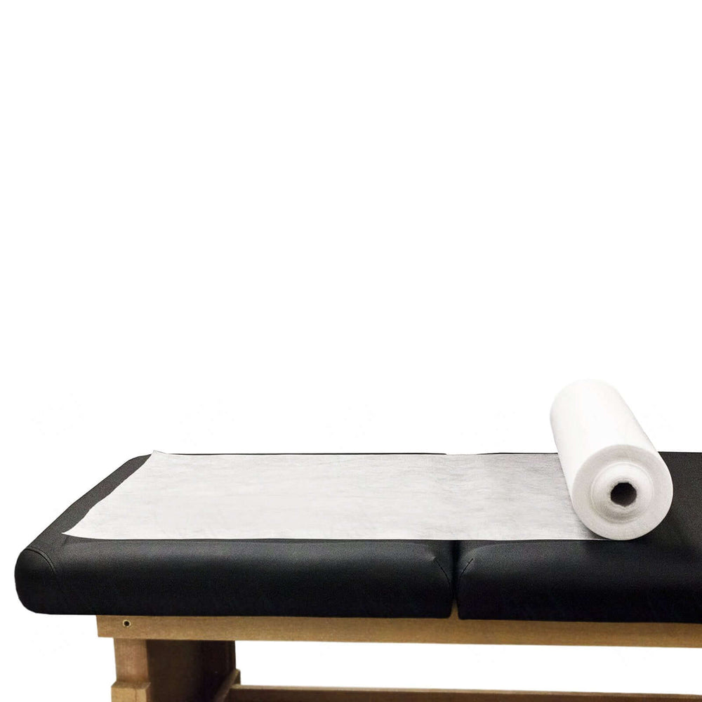 Disposable massage table sheet cover roll on black upholstered table, ideal for affordable and quality DIY spa treatments.