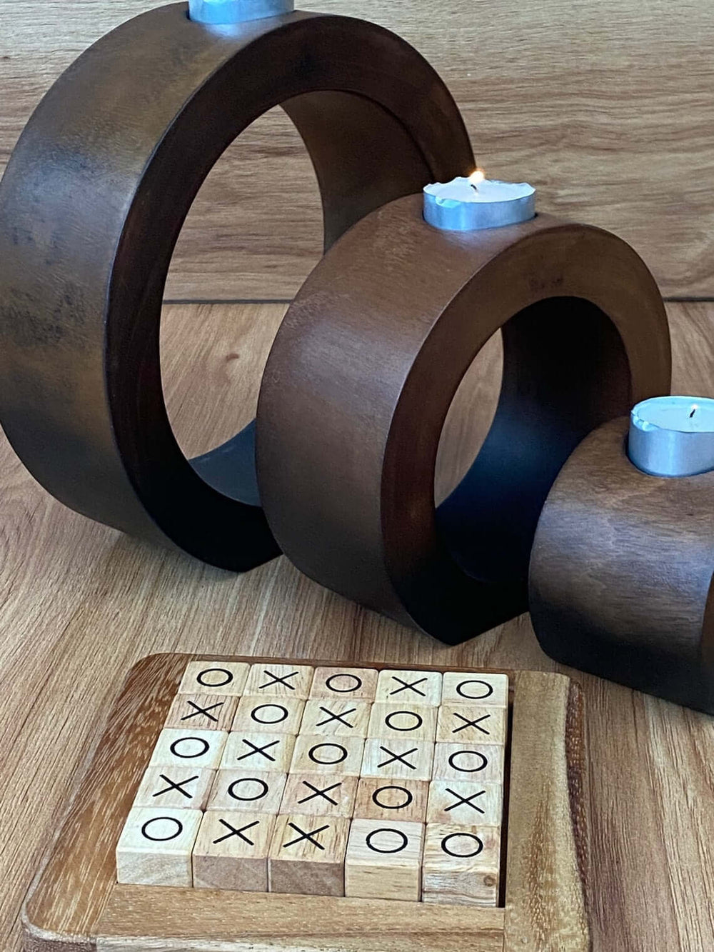 Set of 3 concentric wooden candle holders with tea lights beside a wooden tic-tac-toe board, affordable luxury home decor.