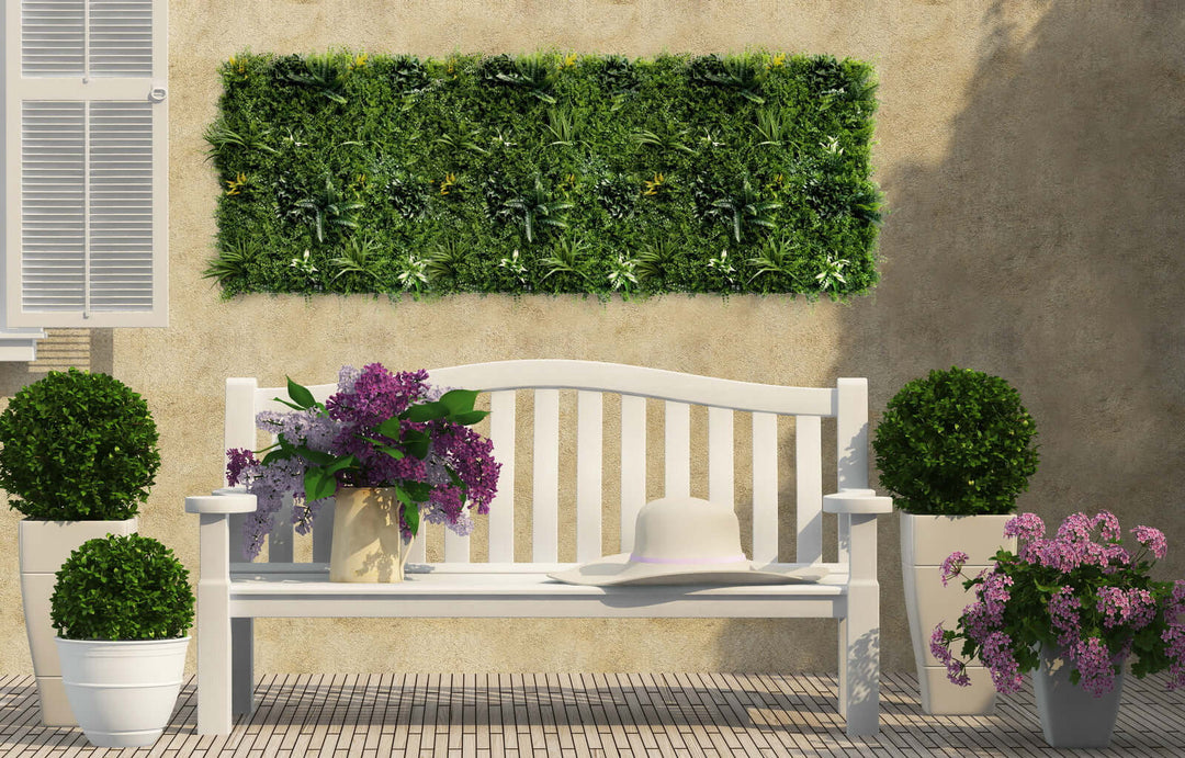 Lush artificial plant wall panel above a white bench in a garden setting with decorative pots and flowers. Affordable DIY decor.