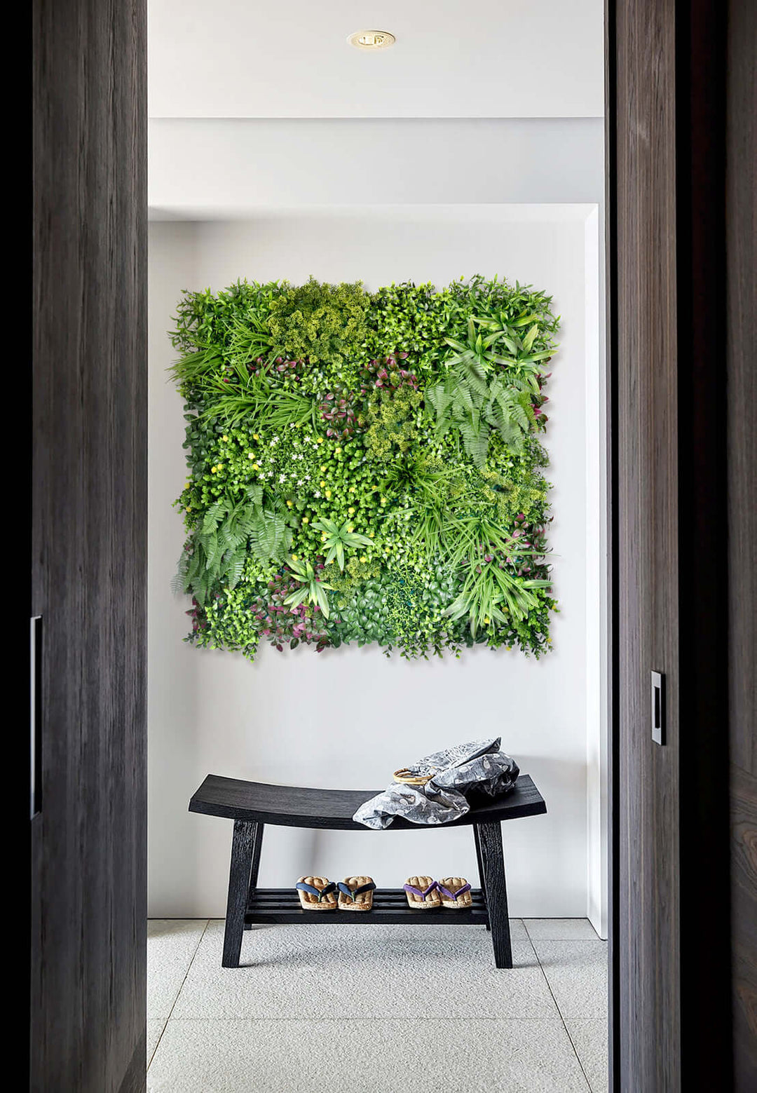 Lush green artificial plant wall panel in modern interior with black bench and decor items. Affordable vertical garden solution.