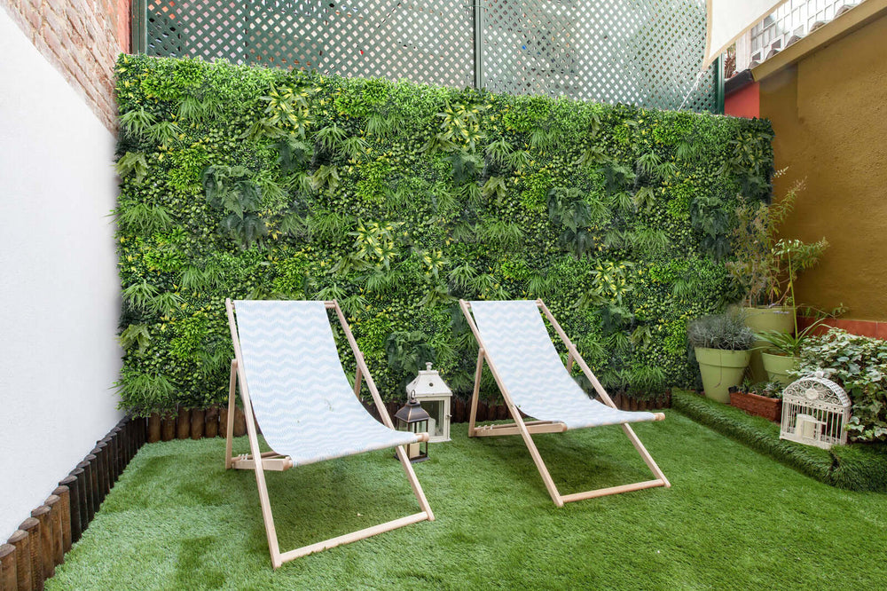 Lush green artificial plant wall with two light blue deck chairs in a cozy outdoor space, showcasing DIY vertical gardening.